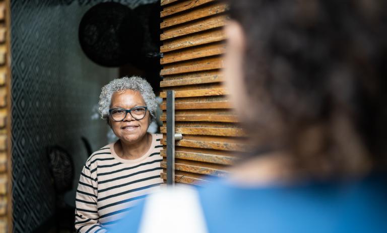 Older woman opening the door to greet a nurse.