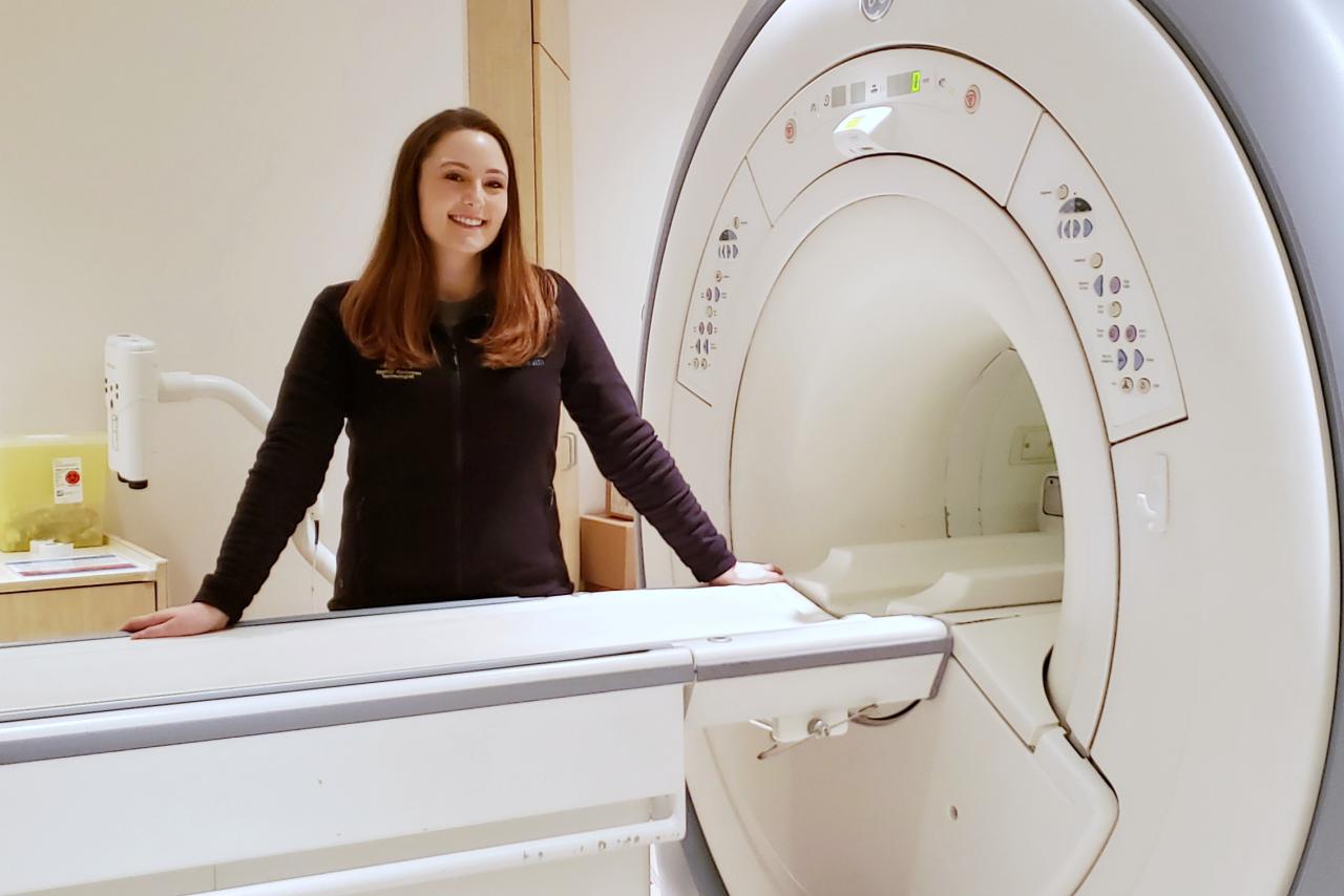 Rebecca Weiss standing behind an MRI machine.