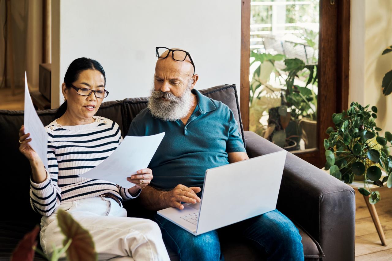 Senior couple using a laptop and reviewing documents on the couch at home.