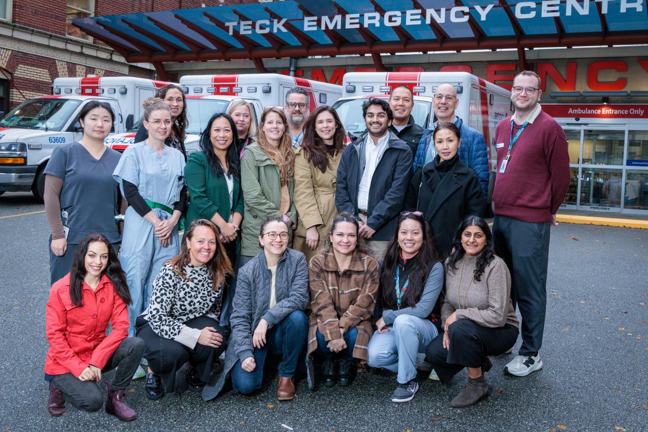 A group of 20 people standing outside an emergency department building