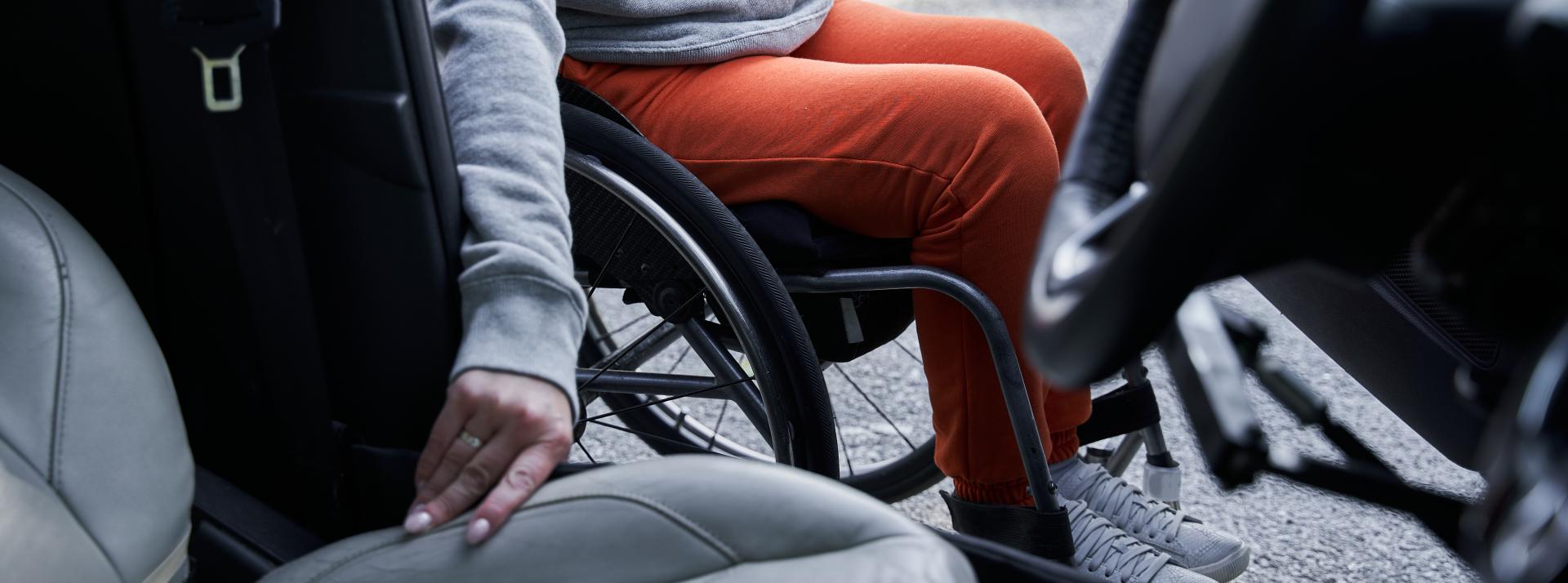 Cropped view of the young disabled person getting out from the car in their wheelchair.