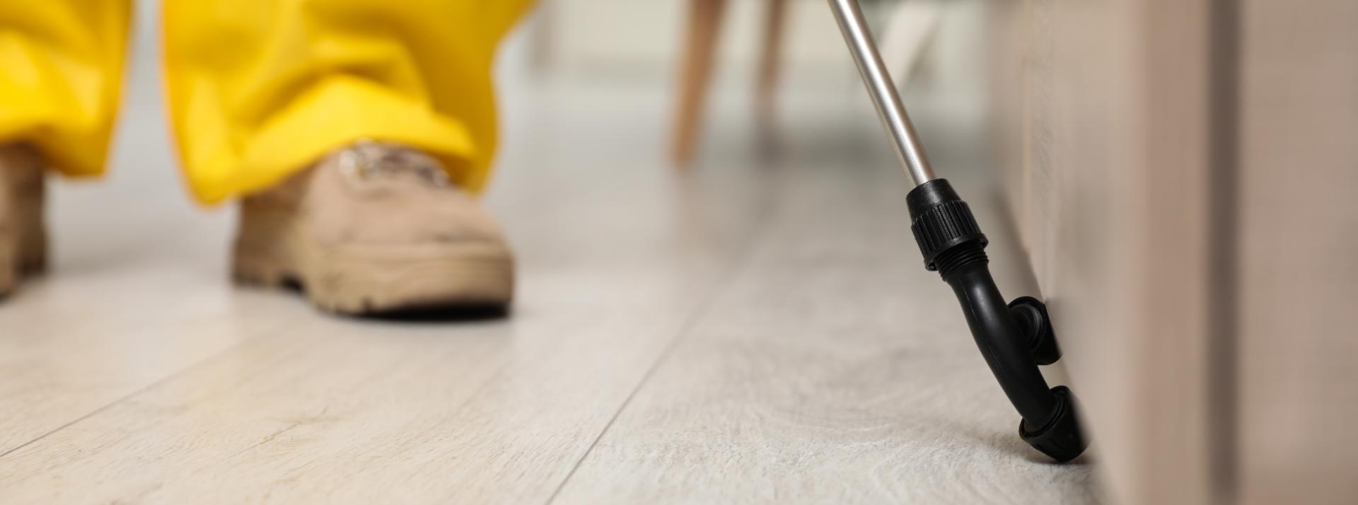 Closup of a pest control worker spraying pesticide around furniture indoors