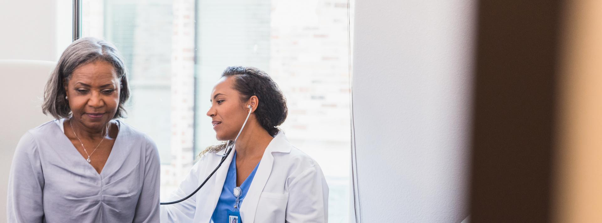  a doctor uses a stethoscope to listen to a senior patient's lungs during a medical exam.