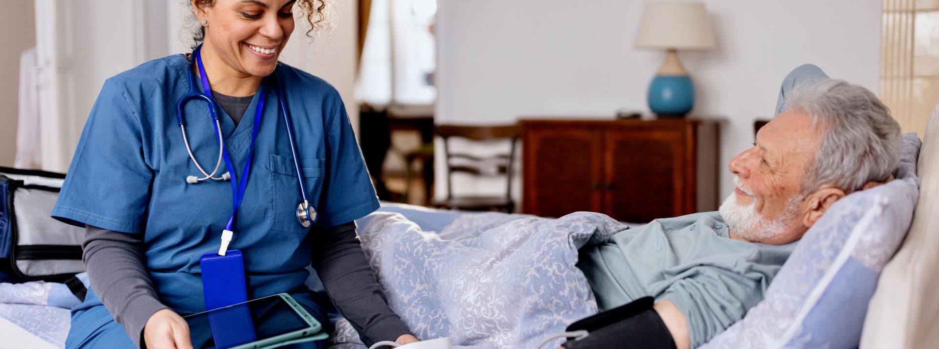 Nurse holding a tablet and caring for an older patient laying on bed