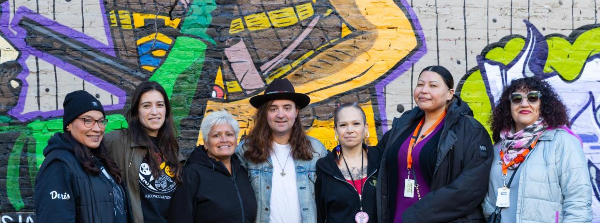 The Indigenous Health Outreach team standing in front of a mural