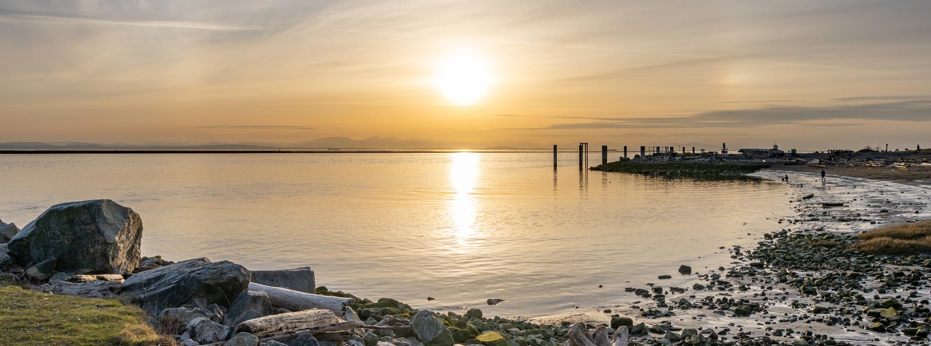 sunset over the Fraser river with a beach and rocks in the foreground