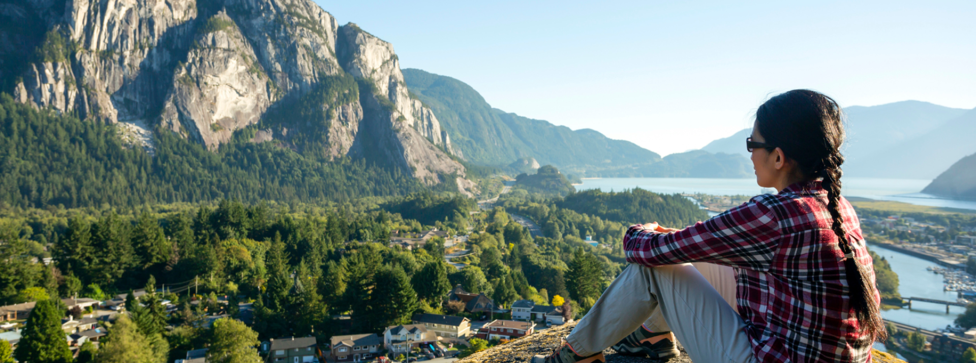 Person sitting on ledge looking out Squamish viewpoint.