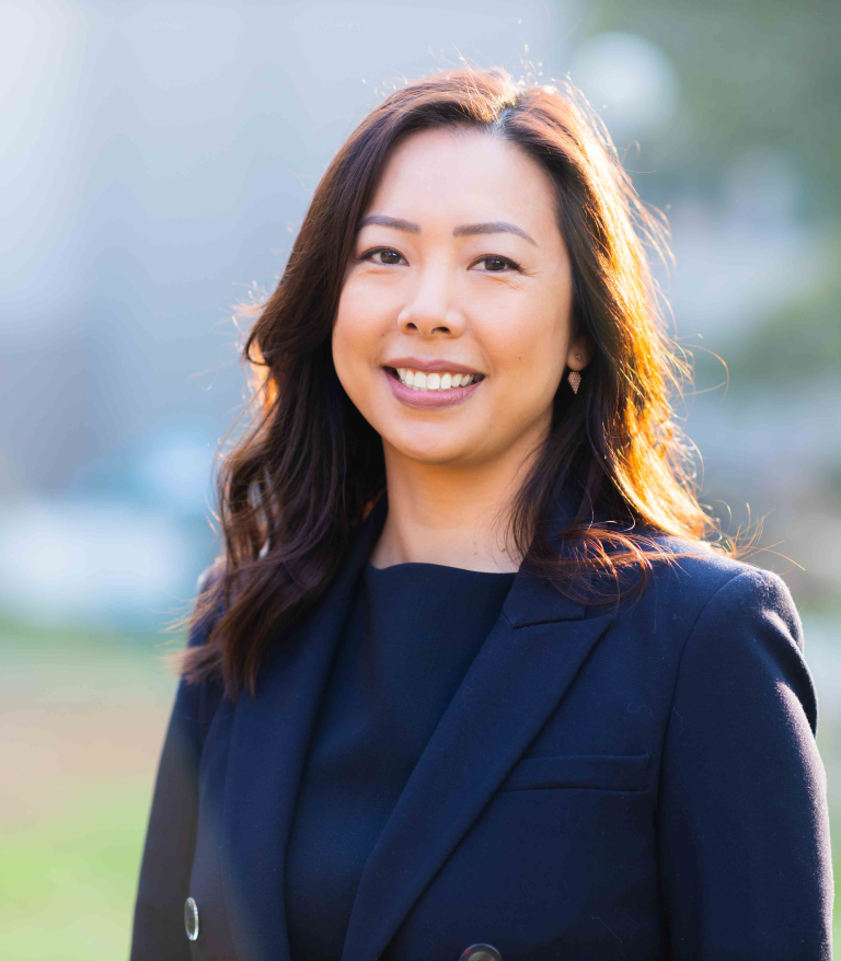 A portrait for Charlene Chiang outside on a sunny day.  She is wearing a dark blue blazer.