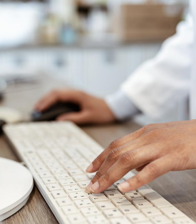 Closeup of pharmacist's hands typing on a computer keyboard at the pharmacy counter