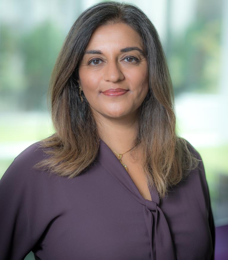 A portrait of Yasmin Jetha indoors.  She is wearing a purple shirt