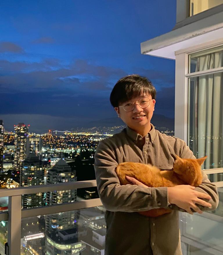 VCH staff member Johnathan standing on a balcony with a cat in his arms.