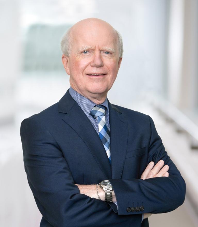 A portrait for Dr. Gavin Stuart in a brightly lit white hallway. He is wearing a dark blue blazer.