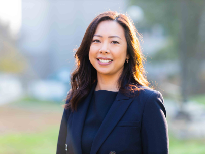 A portrait for Charlene Chiang outside on a sunny day.  She is wearing a dark blue blazer.
