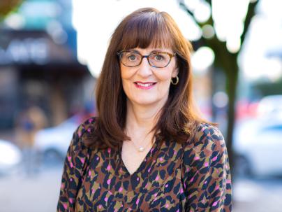 A portrait of Patricia Daly outside on a sunny day.  She is glasses and an animal print blouse