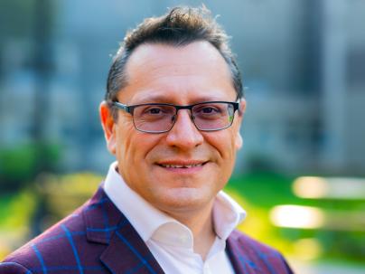 A portrait of Fernando Pica outside on a sunny day.  He is wearing a white shirt and purple blazer