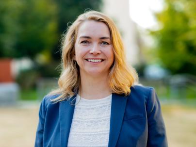 A portrait of Lorraine Blackburn outside on a sunny day.  She is wearing a white shirt and blue blazer.