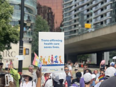 Flags and signs reading “Trans-affirming health care saves lives" and “Vancouver Coastal Health is proud to offer gender-affirming care." 