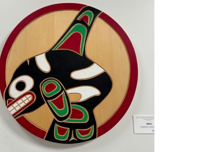 Indigenous wooden carving of an orca mounted on a white wall 