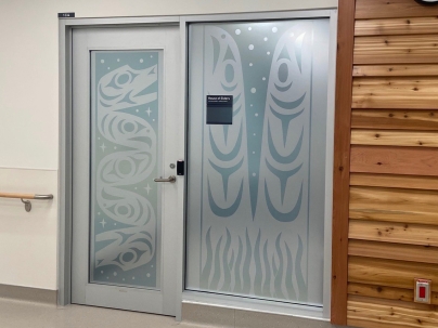 Indigenous artwork of a serpent, salmon and eelgrass mural on top of windows and a door