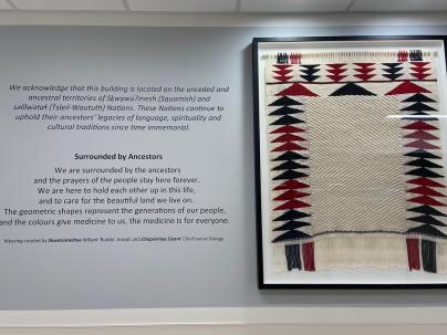 Framed weaving artwork on a white wall in the colours red, black, and cream