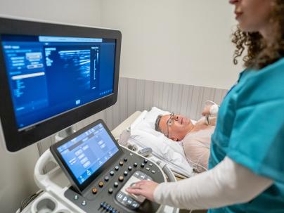 Health care worker in blue scrubs holding a device on a man's chest while looking and an image on screen