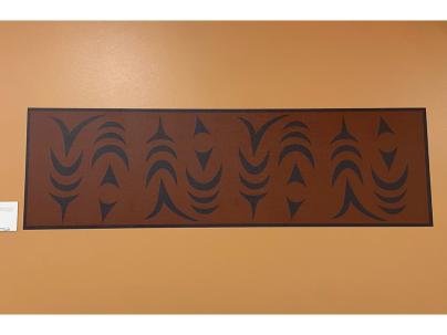 Indigenous artwork in an ochre colour of salmon mounted on a white wall 