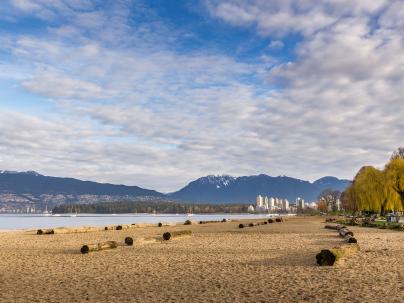 Kitsilano beach with many logs on the sand, with ocean, mountains and downtown vancouver in the background