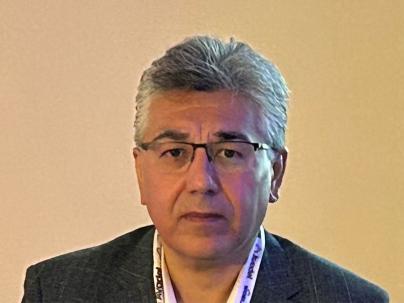 Headshot of a man with a neutral face wearing glasses in front of a yellow background