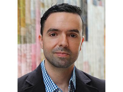 Headshot of a man smiling wearing a dark blazer and blue and white shirt