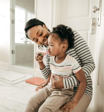 A parent helps their child help their child brush their teeth